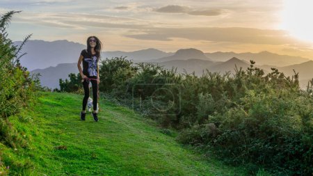 Téléchargez les photos : Femme sereine jouissant de la beauté naturelle vibrante d'une prairie au sommet d'une colline au coucher du soleil - en image libre de droit