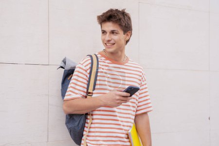 Téléchargez les photos : Jeune homme souriant tenant un cahier naviguant sur Internet avec un téléphone portable - en image libre de droit