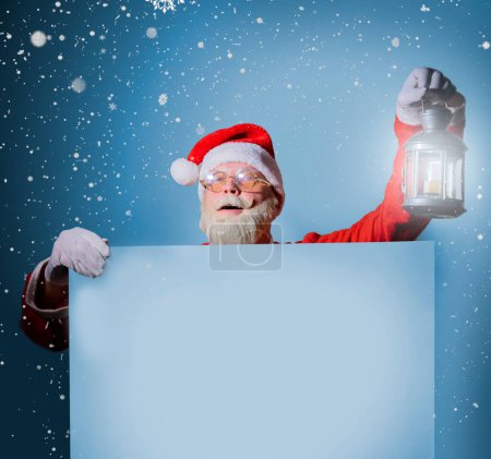 Téléchargez les photos : Père Noël tenant une bannière blanche vierge ou un espace de copie pour le texte, Joyeux Noël et le concept du réveillon du Nouvel An - en image libre de droit