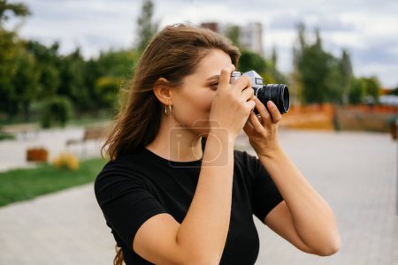 Photo for Beautiful young woman is taking a picture with her vintage camera on a windy day. - Royalty Free Image