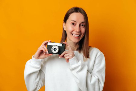 Photo for I love my job as a photographer says a young smiling woman holding a camera over yellow background. - Royalty Free Image