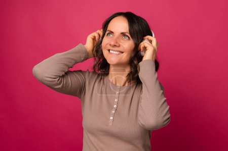 Foto de Alegre mujer de mediana edad con auriculares disfruta escuchando la música sobre fondo rosa. - Imagen libre de derechos