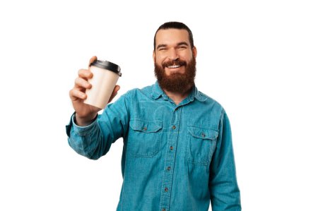 Young wide smiling bearded man is holding a paper take away cup of coffee over white background.
