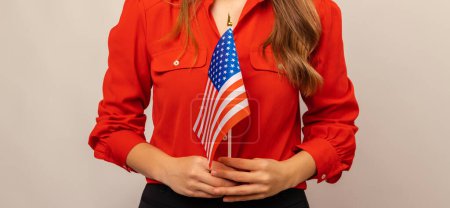 Plan sans visage d'une jeune femme portant une chemise rouge tenant le drapeau des États-Unis avec les deux mains.