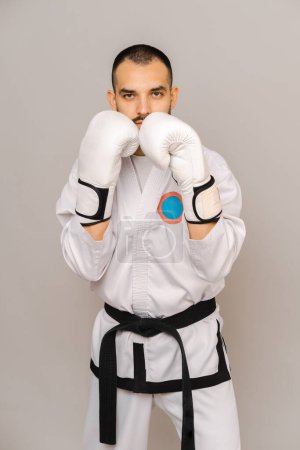 Retrato vertical del estudio de un joven con traje y guantes de artes marciales. Listo para luchar.