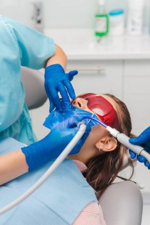 Photo for Dentist is working and making the treatments on a patient wearing rubber dam and red protection glasses. - Royalty Free Image