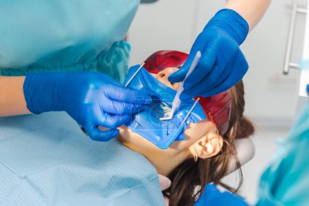 Le dentiste travaille et effectue les traitements sur un patient portant une digue en caoutchouc et des lunettes de protection.
