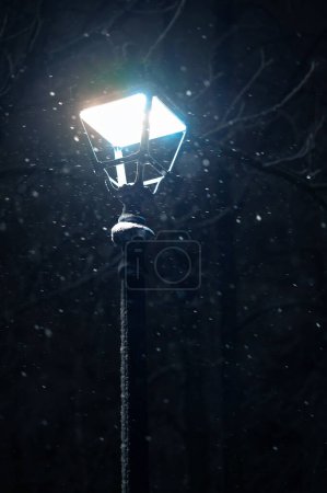 Close up outdoors shot of a street lamp turned on on winter cold snowing night.