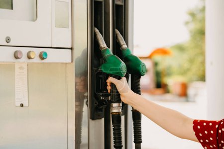 À une station-service, une main tient une buse de pompe à essence verte, se préparant à ravitailler un véhicule