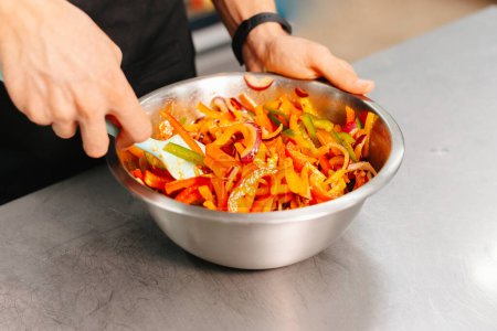 Un chef professionnel qui prépare une salade de légumes frais en mélangeant les ingrédients dans un bol en acier inoxydable sur un comptoir de cuisine