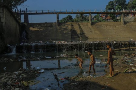 Téléchargez les photos : Trois enfants sont à la recherche de poissons au barrage de Cisadane à Bogor City, dans l'ouest de Java, en Indonésie, le 7 juillet 2019, où l'eau s'était retirée à cause de la sécheresse et était maintenant remplie de déchets - en image libre de droit