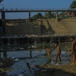 Three kids are searching for fish at the Cisadane Dam in Bogor City, West Java, Indonesia, on July 7, 2019, where the water had receded owing to the drought and was now filled with trash