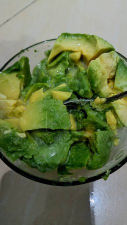Yellow-green avocado pulp cut to small pieces in a glass bowl, view from above
