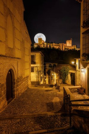 Téléchargez les photos : Une spectaculaire pleine lune se lève sur les anciens murs de l'Alhambra, projetant une lumière magique sur le site historique de Grenade - en image libre de droit