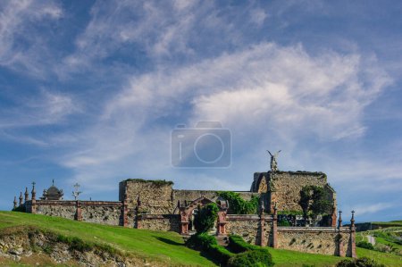 Photo for A commanding angel statue stands atop the ancient stone walls of the historic cemetery in Comillas, under a dynamic sky - Royalty Free Image