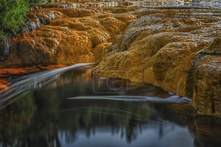Close-up of orange microbial mats over dark flowing waters of Rio Tinto, showcasing natural contrasts