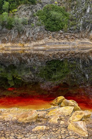 The dramatic red sediments of Rio Tinto contrast sharply with the dark reflective waters and the lush greenery above
