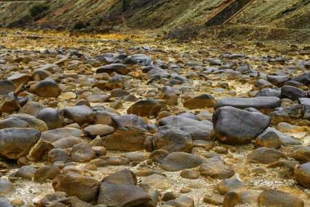 A close view of the yellowish, sulfur-covered rocks in the riverbed of Rio Tinto under a hazy sky