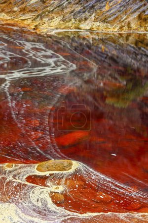 Rich, rust-colored waters of Rio Tinto reflecting the verdant riverside landscape in a serene setting