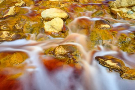 Foaming water rushes over the colorful, iron-laden rocks in the Rio Tinto river