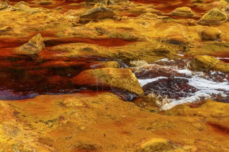 Foaming water rushes over the colorful, iron-laden rocks in the Rio Tinto river