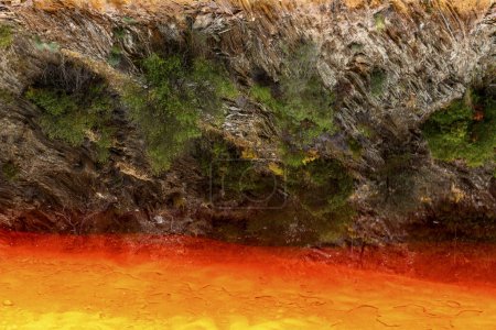 Markante Erdschichten und ein kräftiger Streifen rotes Wasser säumen den rissigen Boden des Rio Tinto