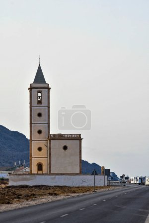 The striking silhouette of a standalone church tower rises along the road near Cabo de Gata, set against a mountainous backdrop.