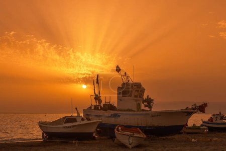 Golden sunset skies illuminate fishing boats moored on a tranquil beach, creating a picturesque end-of-day scene