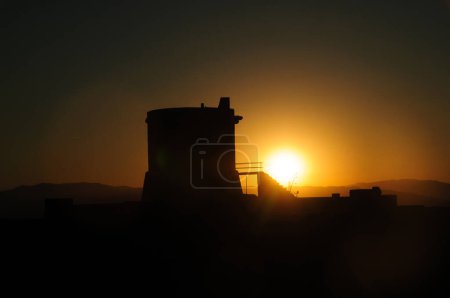 Die Sonne geht hinter dem Torreon de San Miguel del Cabo de Gata unter und wirft eine dramatische Silhouette vor den orangen Himmel