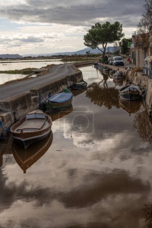 Traditional wooden boats moored along a canal, with the rustic charm of Albufera Valencia's township lining the shores