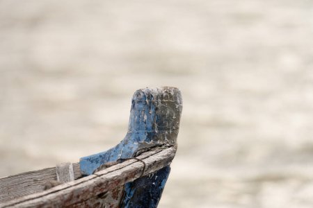 The bow of an old blue boat shows its textured history and character, set against the soft-focus backdrop of a rippling water surface