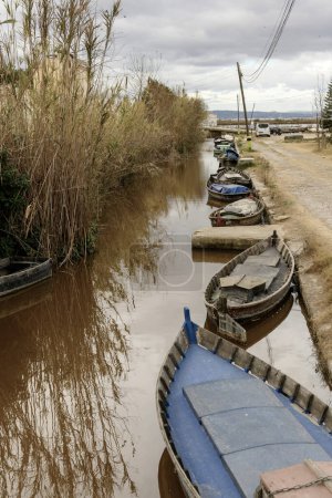 Traditional wooden boats moored along a canal, with the rustic charm of Albufera Valencia's township lining the shores