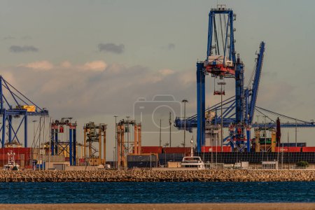 A bustling industrial port shows the activity of trade with container cranes ready to load and unload cargo from container ships.