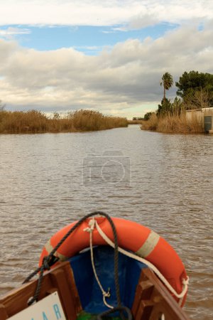 View from a boat gliding through the calm waterways of Albufera Valencia, lined with reeds and a cloud-dappled sky above