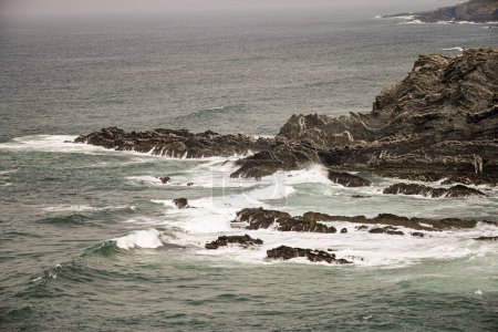 Majestuosos acantilados en Cabo Sardao, Portugal, con formaciones rocosas escarpadas y olas que se estrellan contra la costa. Un cielo parcialmente nublado realza el dramático paisaje costero.