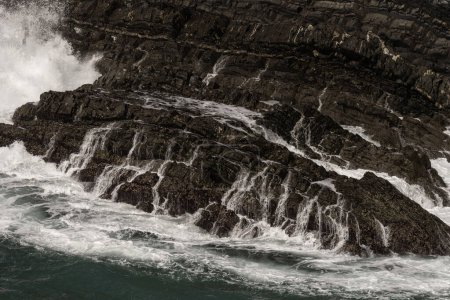 Nahaufnahme von Wellen, die bei Cabo Sardao, Portugal, heftig gegen schroffe Felsen krachen. Turbulente Meeres- und Felsformationen schaffen eine dynamische und kraftvolle Szenerie.