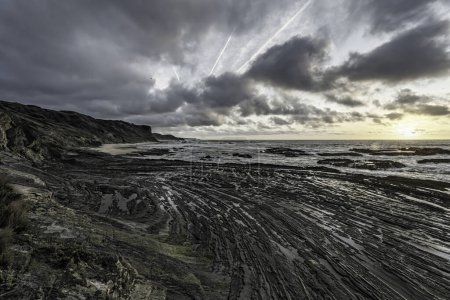 Cielo mohoso con formaciones de nubes dramáticas sobre la playa de Carriagem, Portugal. Formaciones rocosas y costeras crean una escena impactante y atmosférica al atardecer.