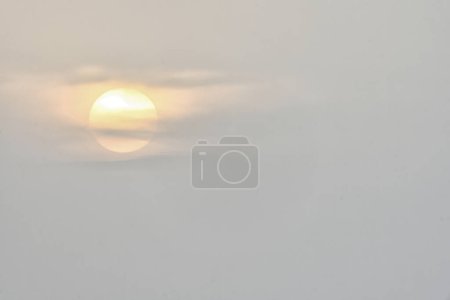 A serene scene of the sun partially obscured by soft clouds during dusk, casting a warm glow through the misty sky.