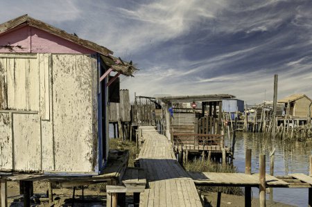 A weathered wooden pier and small hut extend into a tranquil river, with a lone boat anchored nearby.