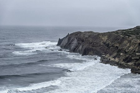 Scenic view of the rugged cliffs and the Atlantic Ocean at Cabo San Vicente, Portugal. The unique rock formations and misty atmosphere create a dramatic coastal landscape.