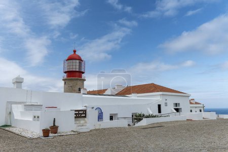 The entrance to Saint Vincent Lighthouse on Cabo de Sao Vicente, Portugal. The lighthouse, surrounded by historic stone walls, stands against a backdrop of blue sky and ocean.