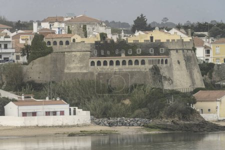 The Fort of San Clemente stands prominently in a picturesque coastal town in Portugal, with charming white buildings and lush greenery by the water.