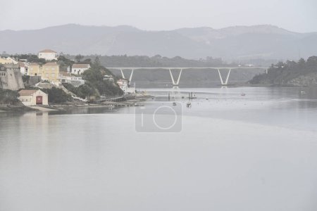 Malerische Szenerie von Rio Mira in Portugal mit einer charmanten Küstenstadt mit historischen Gebäuden und einer modernen Brücke über den ruhigen Fluss.