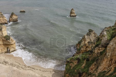Scenic view of the rocky cliffs and sea stacks at Camilo Beach in Portugal. The rugged coastline features dramatic rock formations and a sandy beach.