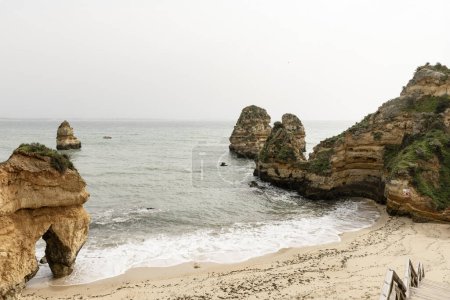 Scenic view of the rocky cliffs and sea stacks at Camilo Beach in Portugal. The rugged coastline features dramatic rock formations and a sandy beach.