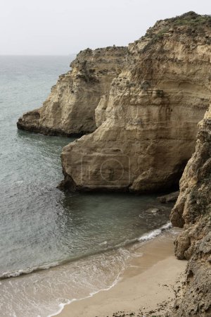 Blick auf die schroffen Klippen und einen einsamen Sandstrand am Camilo Beach, Portugal. Die dramatischen Felsformationen und das klare Wasser unterstreichen die natürliche Schönheit der Küste.
