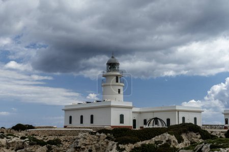 The Faro de Cavalleria lighthouse stands majestically against a backdrop of dramatic clouds in Menorca. This iconic landmark overlooks the rugged coastline.