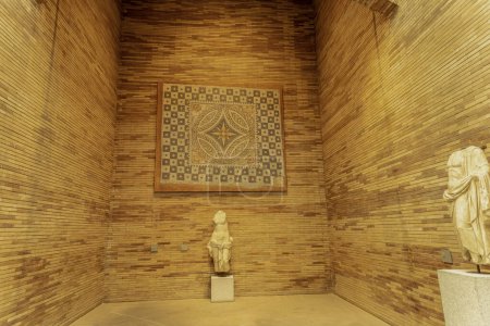 An exhibit featuring an intricate ancient mosaic displayed on a wall with two marble statues in a museum.
