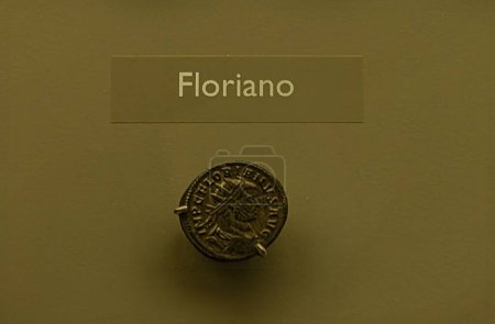 Detailed view of a bronze coin featuring the profile of Roman Emperor Florianus. The coin is part of a museum exhibit highlighting ancient Roman currency.