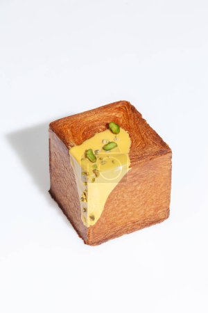 Foto de Croissant crujiente recién horneado en forma de cubo rematado con crema de pistacho dulce y migas de nuez aisladas sobre fondo blanco. Deliciosa pastelería estilo francés viennoiserie - Imagen libre de derechos